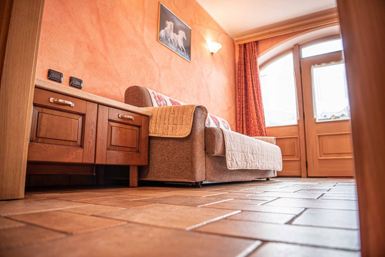 Ein gemütliches Zimmer mit einer Couch, Holzschränken, einer Wandleuchte und einem Fenster mit Vorhängen.