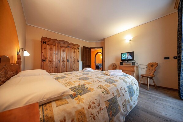 Hotellihuone, jossa on suuri sänky, puinen vaatekaappi, televisio ja pieni tuoli.
