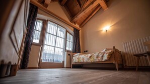 Une chambre à coucher avec un lit en bois, une chaise, un radiateur et une fenêtre avec des rideaux.
