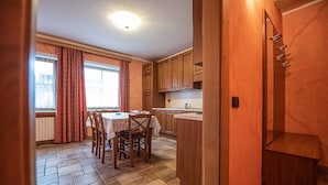 Une cuisine avec des meubles de rangement en bois, une table à manger avec des chaises et une fenêtre avec des rideaux.