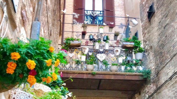 En smal passage med en balkon pyntet med plantekasser og blomster.