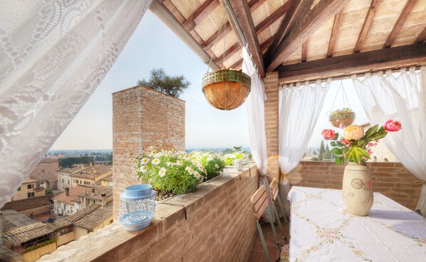A balcony with a view of a cityscape, a hanging basket, a vase with flowers, and a decorative lantern.