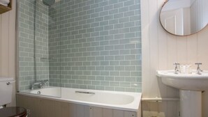 A bathroom with a white bathtub, a white sink, and a mirror on the wall. - The Elephant at the Market (Newbury)