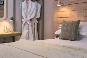 Una habitación de hotel con una cama, una mesita de noche con lámpara, un espejo y una bata colgada en la pared.