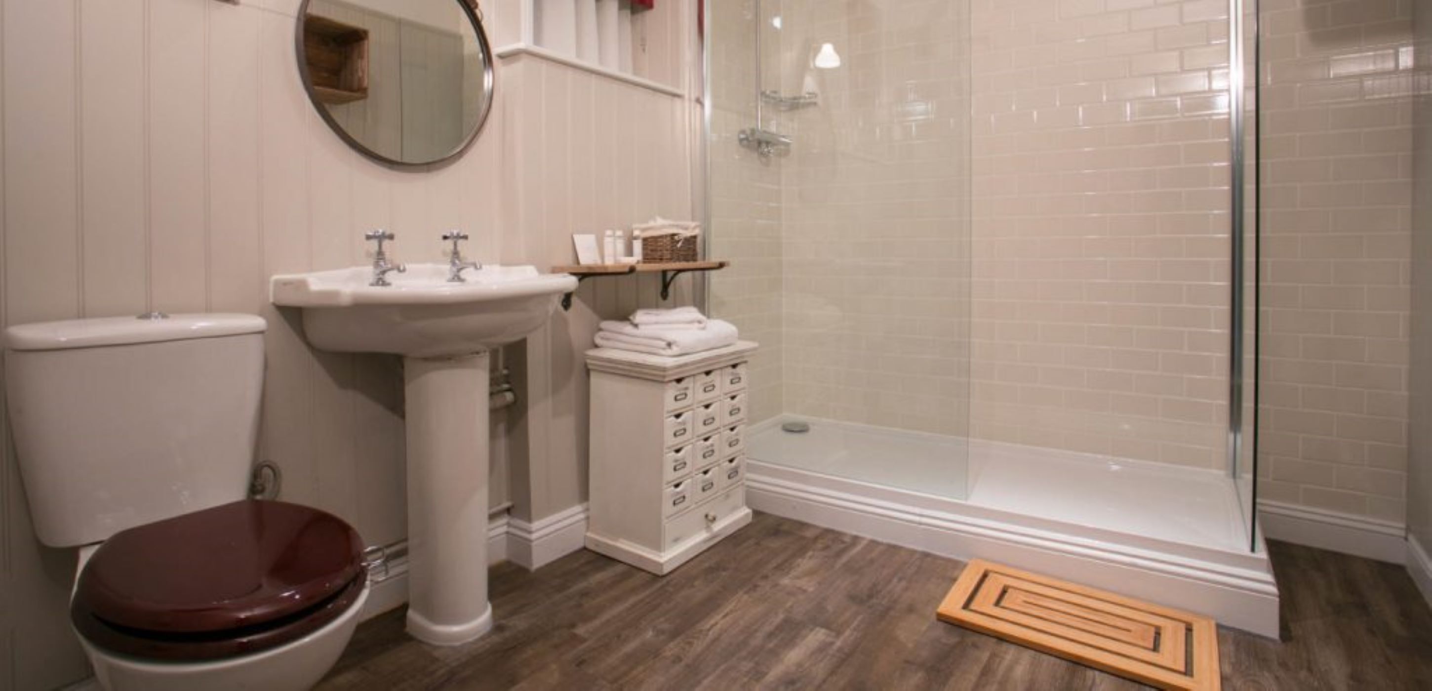 Baño con inodoro, lavamanos pedestal y ducha con mampara de vidrio.