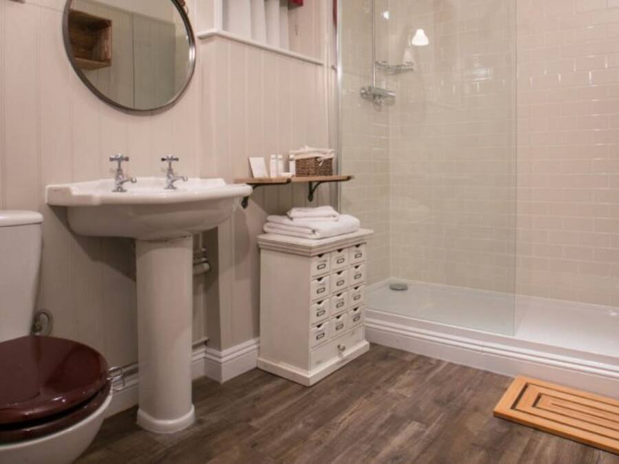Baño con inodoro, lavamanos pedestal y ducha con mampara de vidrio.