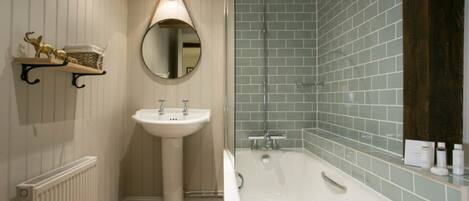 Un baño con lavamanos pedestal, un espejo redondo, una bañera y un estante con artículos de aseo.