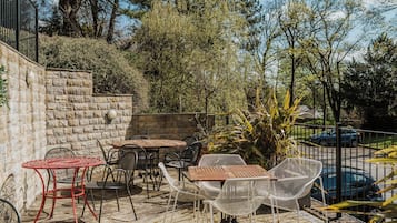An outdoor patio with stone walls, metal tables and chairs, and a view of a street with cars.