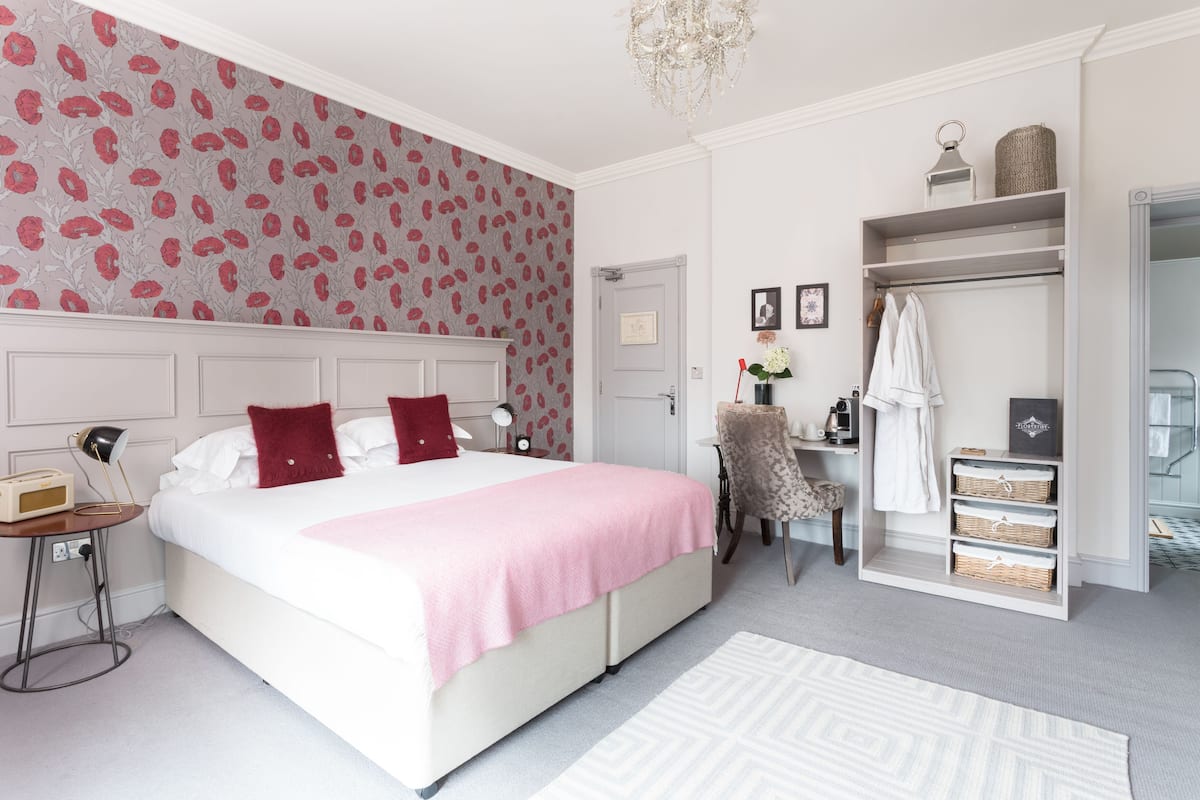 A bedroom with a large bed, a chair, a desk, and a wardrobe.