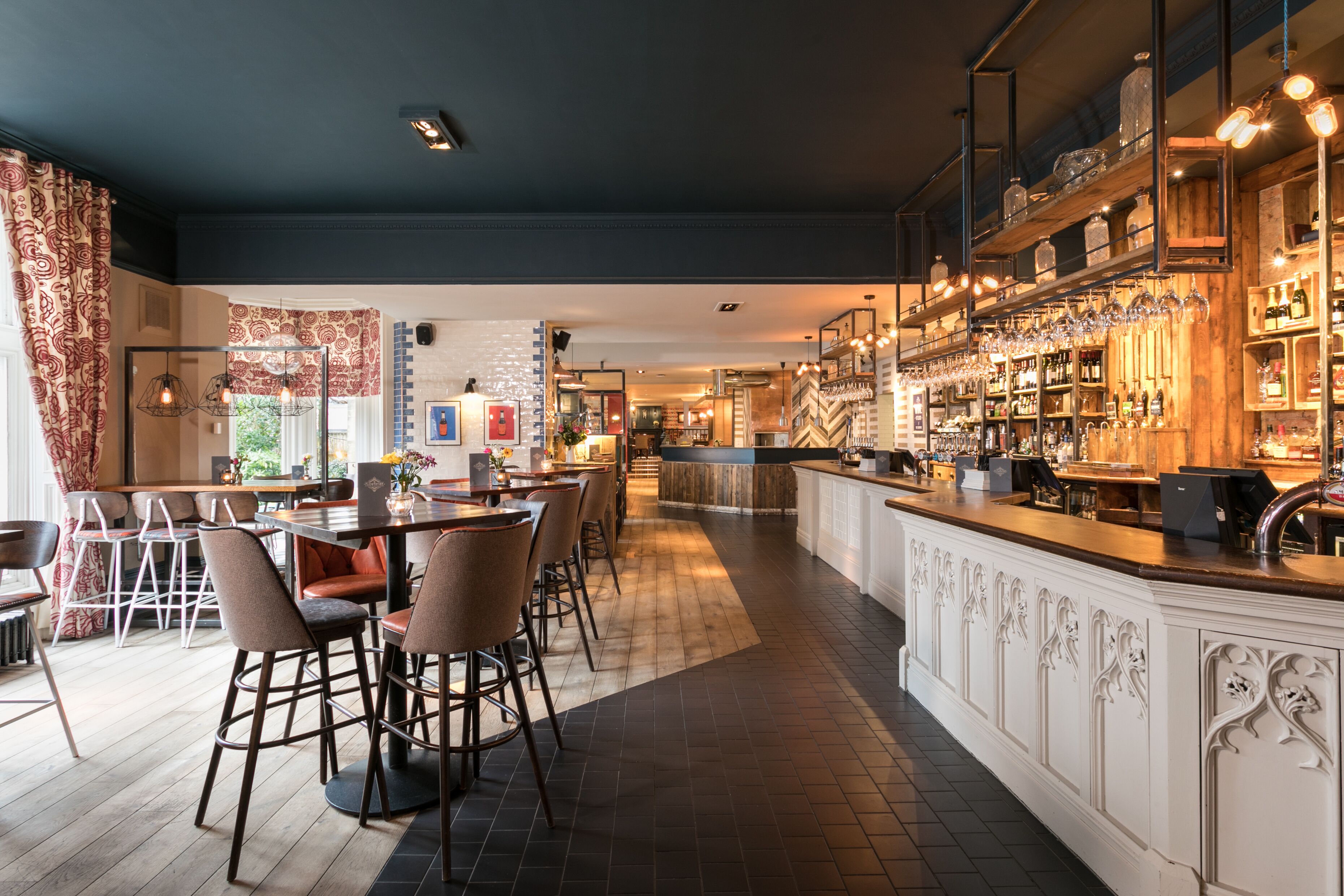 A modern bar area with a long counter, bar stools, and shelves stocked with bottles.