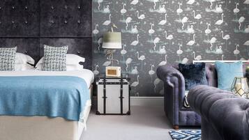 A bedroom with a bed, a dresser, a nightstand, a lamp, and a patterned wallpaper.