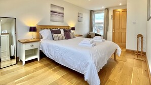 Une chambre à coucher avec un grand lit, des tables de chevet, un miroir et une fenêtre avec des rideaux.