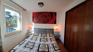 A bedroom with a bed, a large red rose painting on the wall, bedside lamps, and a window with a view of greenery. - Azalea Residence (Orta San Giulio)