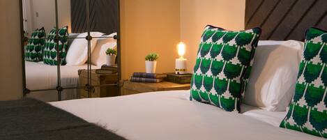 A hotel room with a large bed, a bedside table with a lamp, a mirror, and decorative pillows.