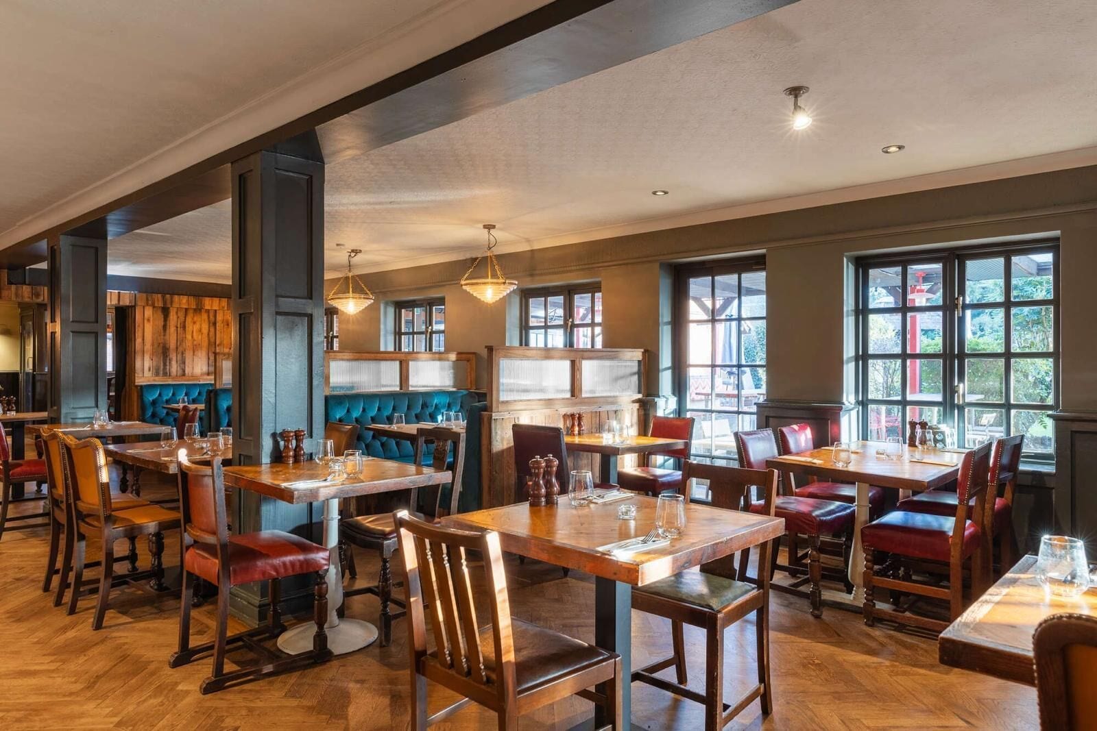 Een restaurant met houten tafels en stoelen, blauwe met kussens uitgeruste zitjes en grote ramen met uitzicht op het omliggende landschap.