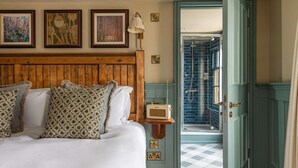 A bedroom with a wooden headboard, a bed with patterned pillows, a bedside radio, and a view of a bathroom with a blue-tiled shower. - Huntsman of Brockenhurst (Brockenhurst)