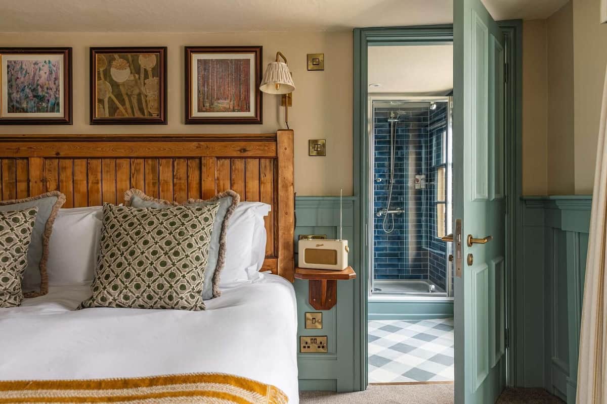A bedroom with a wooden headboard, a bed with patterned pillows, a bedside radio, and a view of a bathroom with a blue-tiled shower.