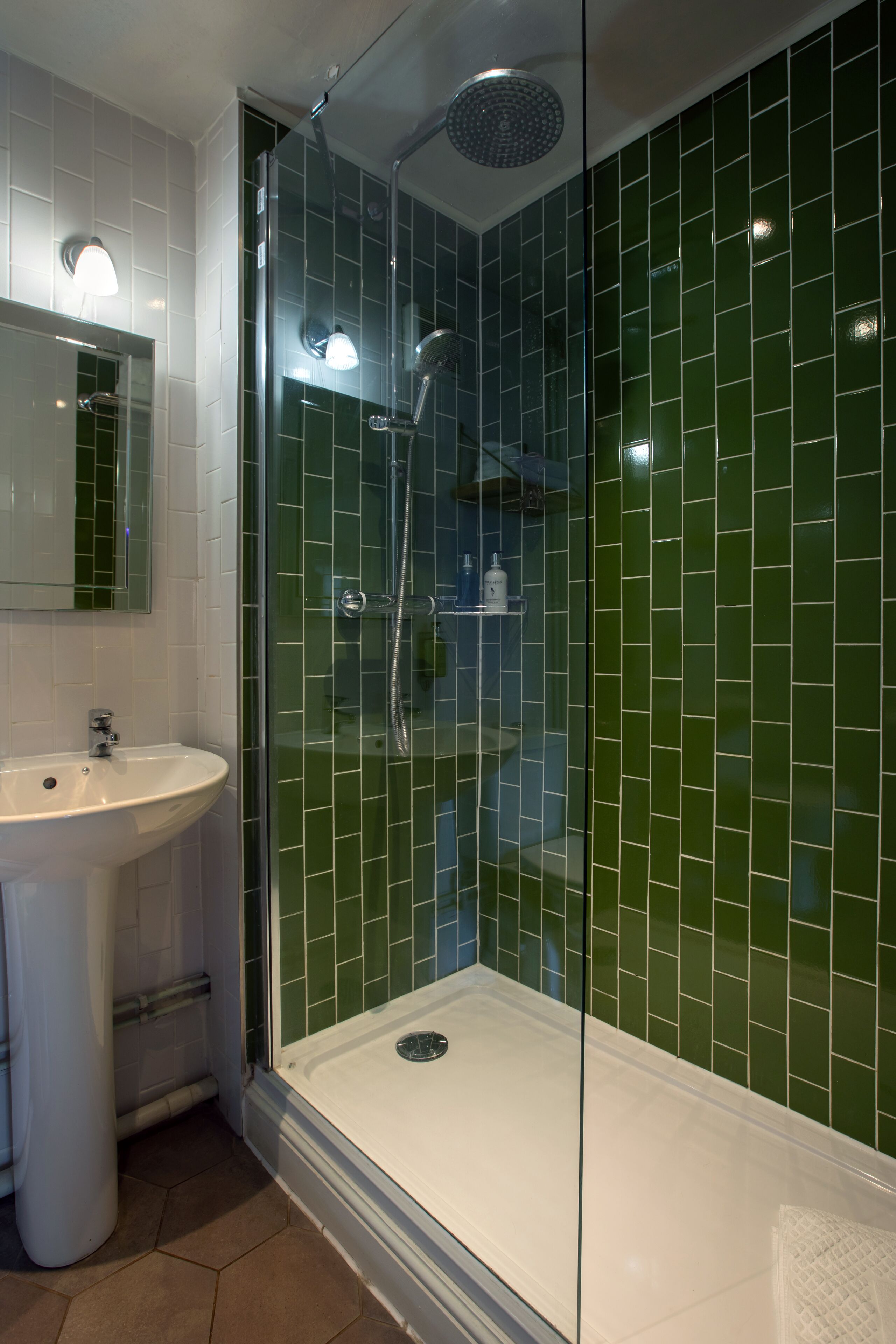 A modern bathroom with a glass-enclosed shower, a white sink, and green-tiled walls.