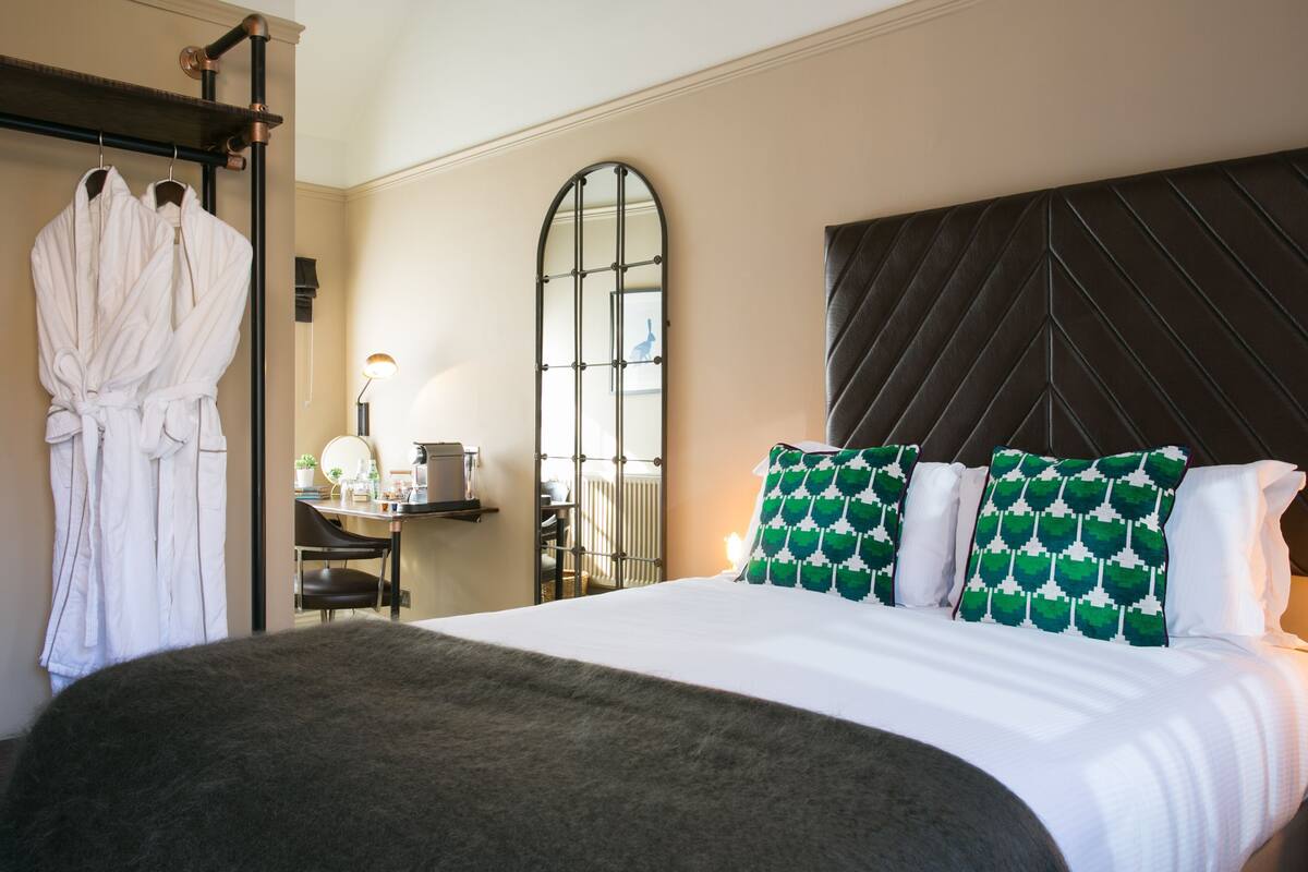 A hotel room with a bed, a mirror, a chair, and two robes hanging on a rack.