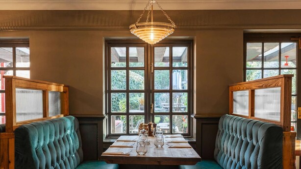 A dining area with a wooden table and two green upholstered booths. - Huntsman of Brockenhurst (Brockenhurst)