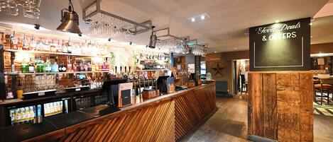 A bar area with a wooden counter, shelves with bottles, and a sign indicating food deals and offers.