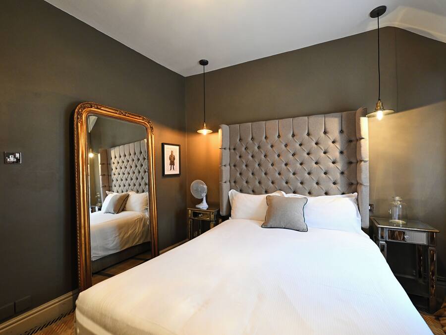 A bedroom with a large bed, a mirror, a bedside table, and a lamp.