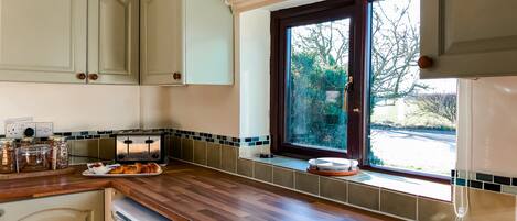 Une cuisine avec des plans de travail en bois, une fenêtre donnant sur les arbres et un grille-pain posé sur le plan de travail.