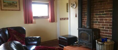 Een woonkamer met een zwarte leren bank, rode kussens, een open haard en een raam met gordijnen.