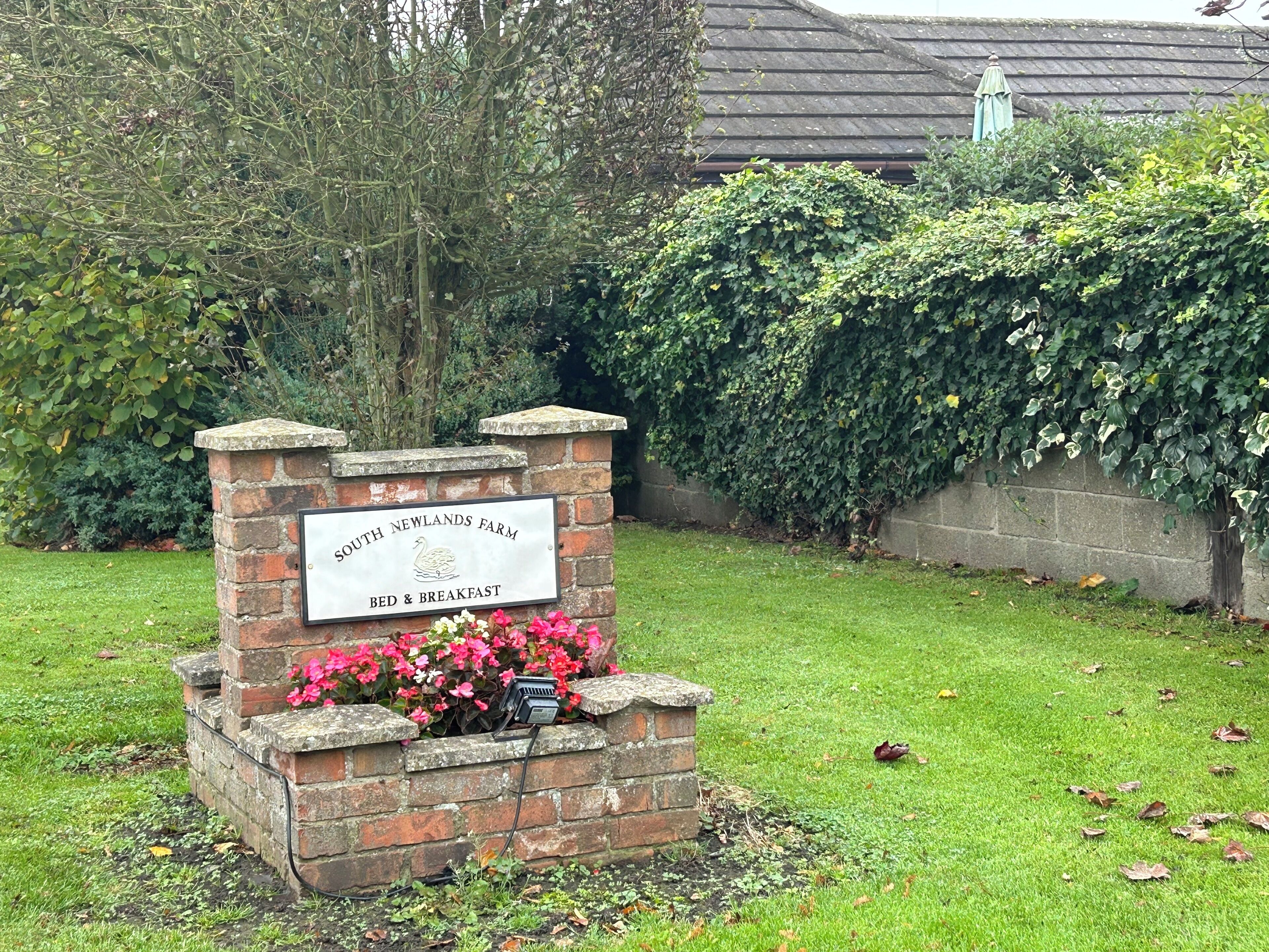 A sign for South Newlands Farm Bed & Breakfast with a brick base and a plaque.