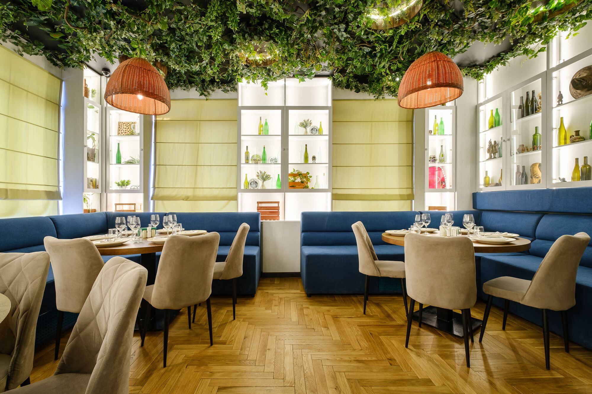 A restaurant with blue seating, wooden herringbone flooring, and green foliage on the ceiling.
