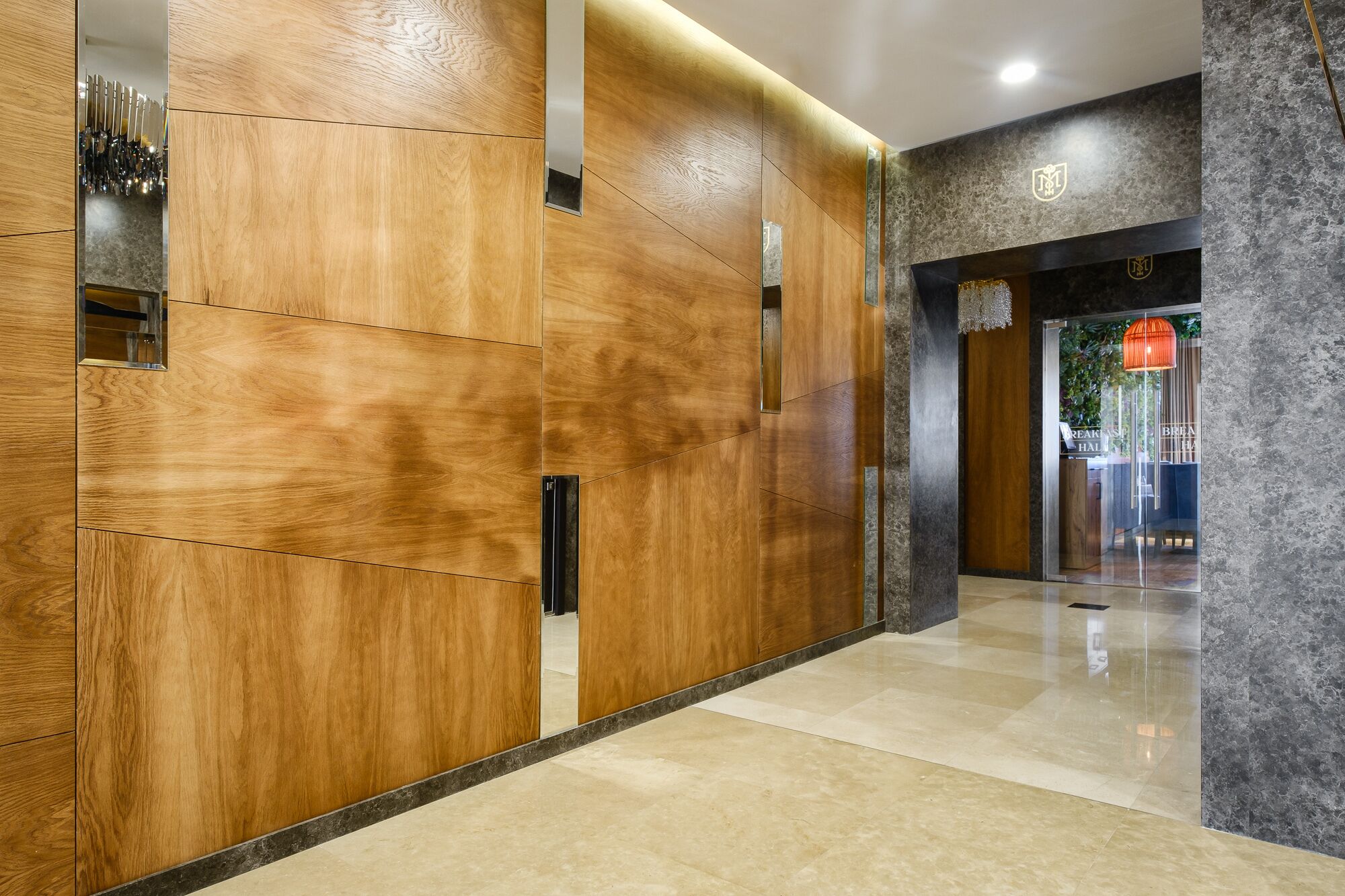 Un moderno vestíbulo de hotel con paneles de madera y una entrada de vidrio que da a un área de desayuno.