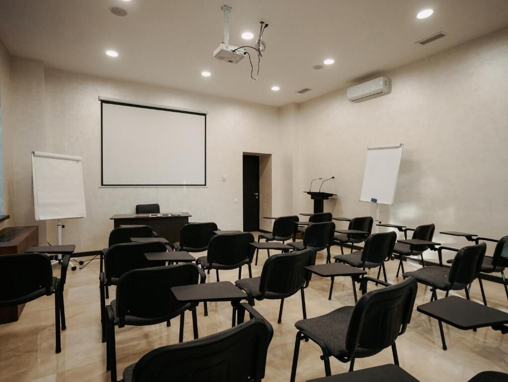 Un salón de conferencias con un proyector, una pizarra y filas de sillas.