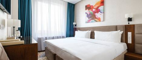 Ein Hotelzimmer mit einem großen Bett, einem Schreibtisch mit Lampe, einem Sessel und einem Gemälde an der Wand.