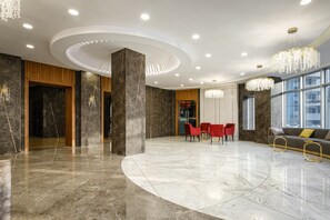 A spacious lobby with a curved marble floor, a central seating area with red chairs, and a chandelier. - Grand Mildom Hotel (Almaty)