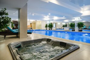 An indoor swimming pool with a hot tub, lounge chairs, and potted plants. - Grand Mildom Hotel (Almaty)