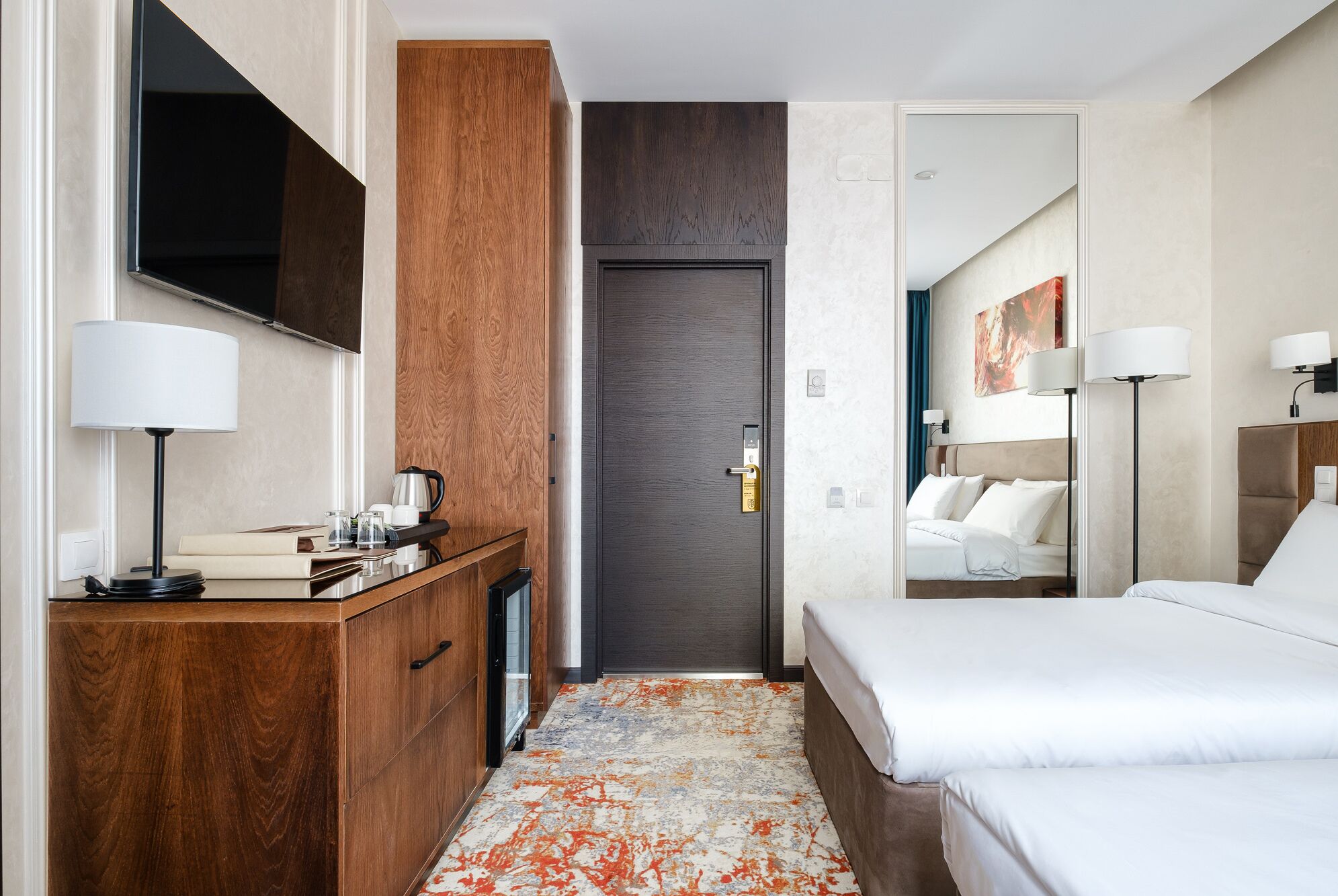 Een hotelkamer met een houten bureau, een bed, een spiegel en een deur naar een andere kamer.
