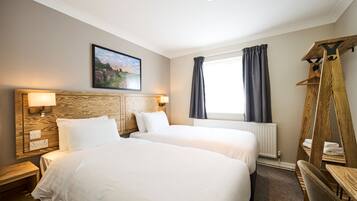 A hotel room with two beds, a wooden headboard, a painting, a window with curtains, and a wooden coat rack.