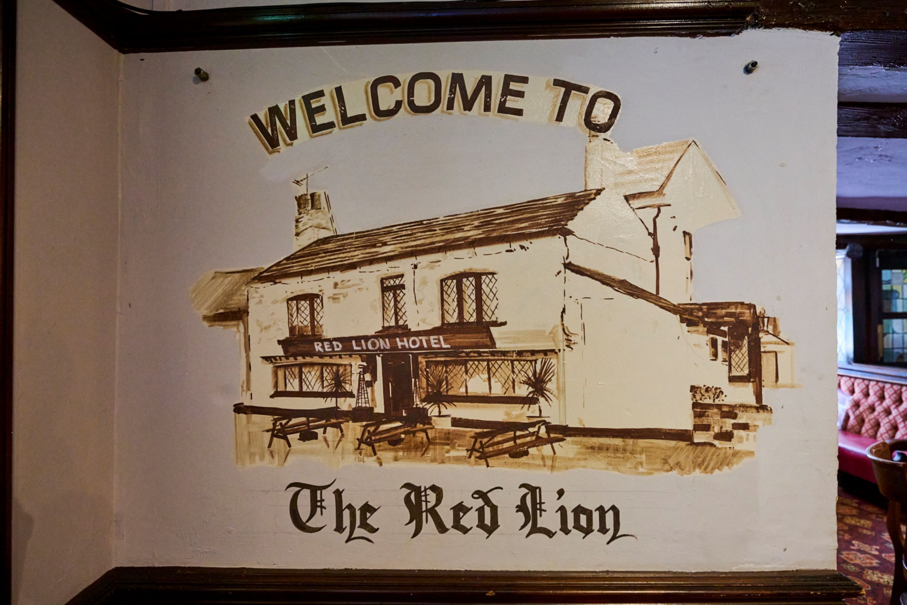 A sign with "WELCOME TO The Red Lion" and a depiction of a building with a sign reading "Red Lion Hotel".