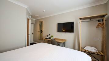 Habitación de hotel con una cama grande, un escritorio con silla, un televisor de pantalla plana en la pared y un perchero de madera con una toalla.