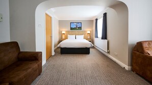 Een hotelkamer met een groot bed, twee nachtkastjes met lampen, een hoofdeinde, een raam met gordijnen en een tapijtvloer.