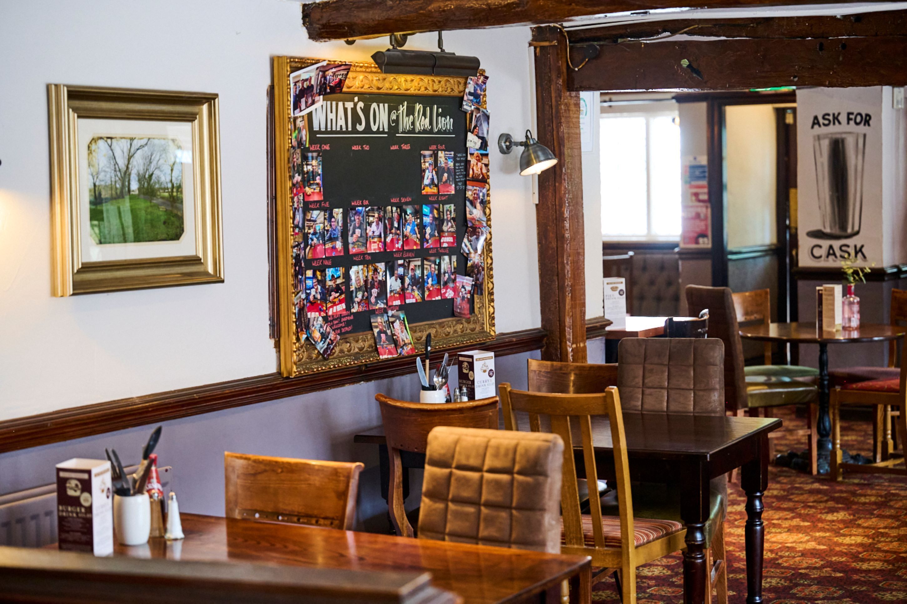 A cozy restaurant interior with wooden furniture, a wall-mounted photo collage, and a 'CASK' sign.
