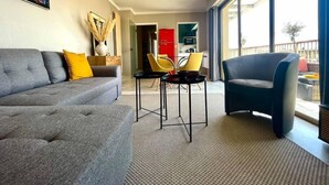 A modern living room with a grey sofa, a blue armchair, and a small table. There is a large window providing a view of the outside. - RoofTop Apartment - Quartier Croisette (Cannes)