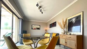A modern dining area with a round table, four yellow chairs, a wooden cabinet, and a large framed artwork on the wall. - RoofTop Apartment - Quartier Croisette (Cannes)