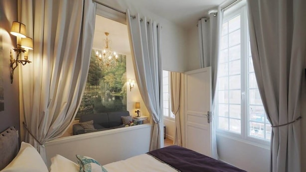 A bedroom with a bed, a window with curtains, a chandelier, and a view of greenery outside. - Louvre Opera Design (Paris)