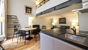 A modern kitchen with a dining area, wooden flooring, and a loft-style ceiling.