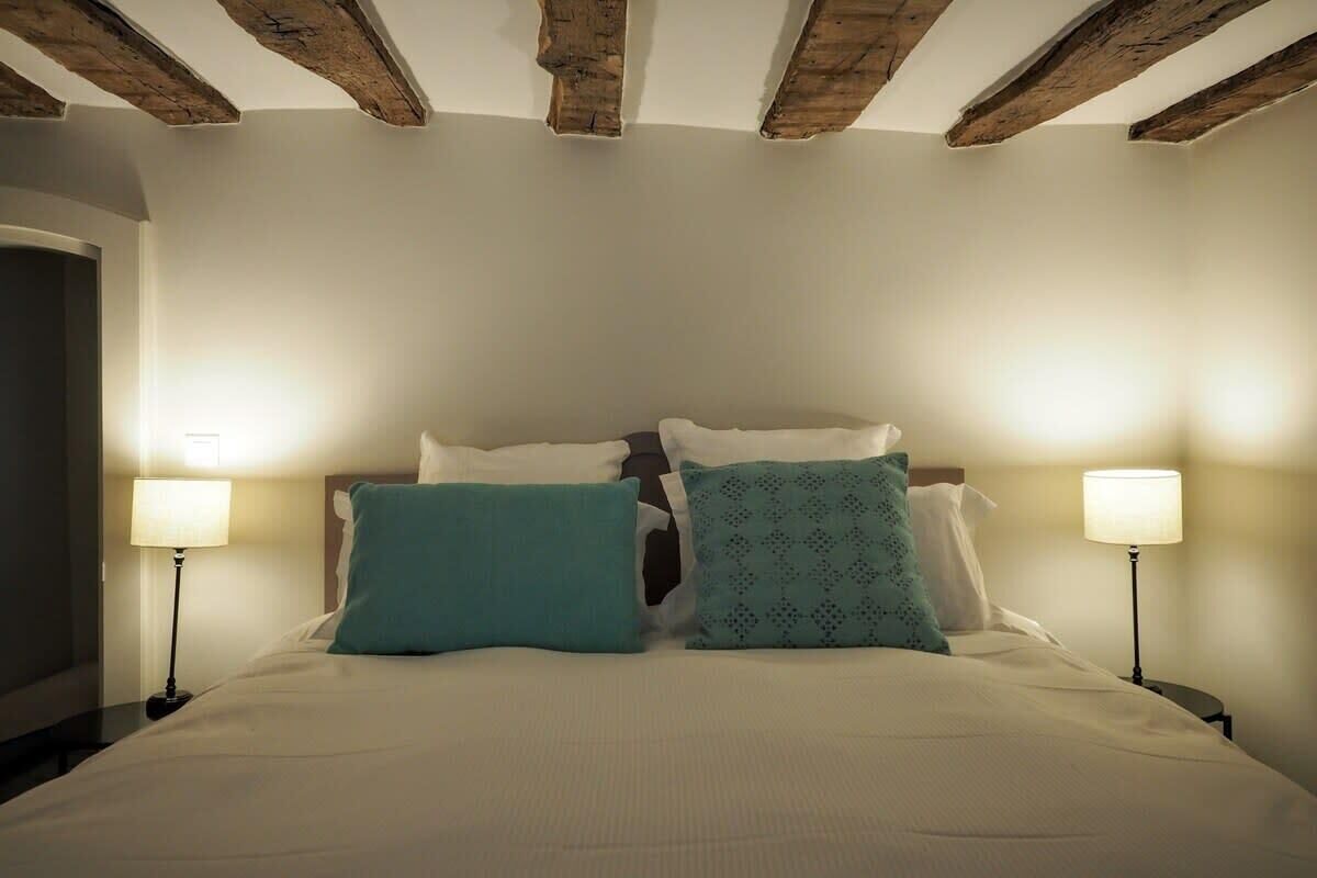 A bedroom with a bed, two bedside lamps, and a wooden ceiling.