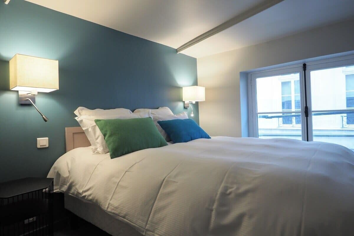A hotel room with a large bed, two wall-mounted lamps, and a window with a view of the outside.