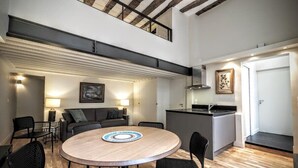 A modern interior with a round wooden dining table, black chairs, a sofa, and a kitchen area.