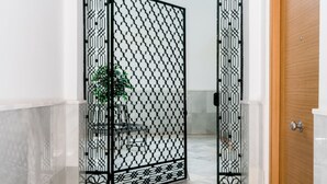 Un couloir avec une grille décorative en métal noir, une porte en bois et un sol en marbre.