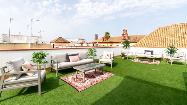 Une terrasse sur le toit avec une pelouse verdoyante, des meubles d’extérieur et une vue sur les bâtiments en arrière-plan.